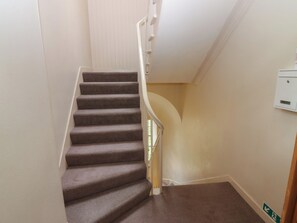 Un escalier recouvert de moquette, avec des rampes blanches et une boîte électrique fixée au mur.