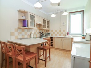 Une cuisine avec des meubles de rangement en bois, un îlot central avec des tabourets, une fenêtre donnant sur un beau paysage et une horloge au mur.