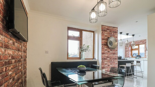 Una cocina moderna con pared de ladrillo, un área de comedor con mesa y sillas de vidrio, y una isla de cocina visible.