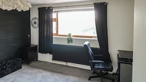 Una habitación con una silla de oficina negra, un radiador, una ventana con cortinas negras y un reloj de pared.