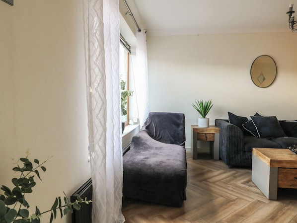 A modern living room with a sofa, a small side table with a plant, and a wooden coffee table. - 57 Howden Avenue (Doncaster)