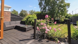 Una terraza con zona de estar, un jardín con plantas en flor y un árbol grande.