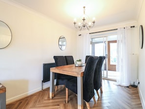 A dining area with a wooden table and black chairs, a chandelier, a radiator, and a large mirror on the wall.