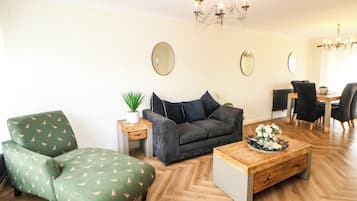 A living room with a sofa, armchair, coffee table, and dining area with chairs.