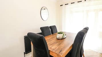 A dining area with a wooden table, black upholstered chairs, a wall-mounted mirror, and a window with curtains.