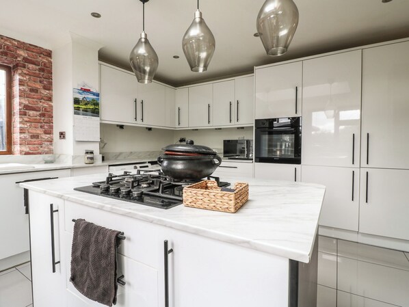A modern kitchen with white cabinets, a central island with a stove, a microwave, and an oven.