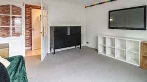 Una habitación con pared de ladrillo, una puerta blanca, un mueble de entretenimiento negro y una estantería blanca, además de un televisor montado.