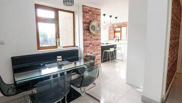 Una cocina moderna con pared de ladrillo, un comedor con mesa y sillas de vidrio, y una isla de cocina visible.