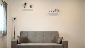 Een grijze bank met kussens, een vloerlamp en twee planken met decoratieve spullen.