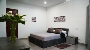 Een moderne slaapkamer met een bed, nachtkastjes, een bloevas en twee kunstwerken aan de muur.