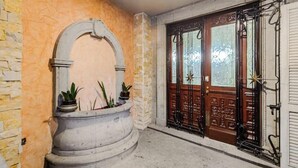 Un mur de pierre surmonté d’une arche circulaire, un pot de fleurs et une porte en bois avec un portail en métal.