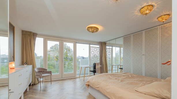Ein Schlafzimmer mit Bett, Kommode, Stuhl und einem Balkon mit Blick.