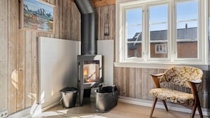 A room with a wood-burning stove, a window with a view of houses, and a chair with a floral pattern.