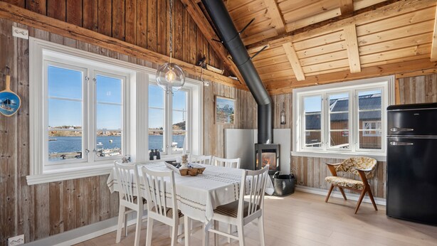 A wooden interior with a dining table, chairs, a black refrigerator, and a fireplace.