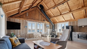 A spacious living area with a wooden ceiling, a dining table, and a kitchen area with a stove and refrigerator.