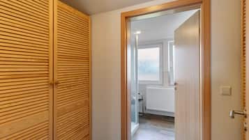 Ein Flur, der zu einem Badezimmer mit Heizkörper, Fenster und einer Tür mit Holzrahmen führt.