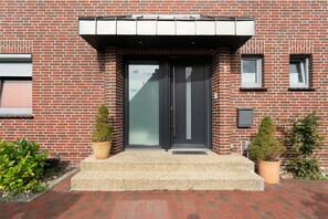 Un edificio de ladrillo con una puerta negra, dos plantas en macetas y un acceso de grava.