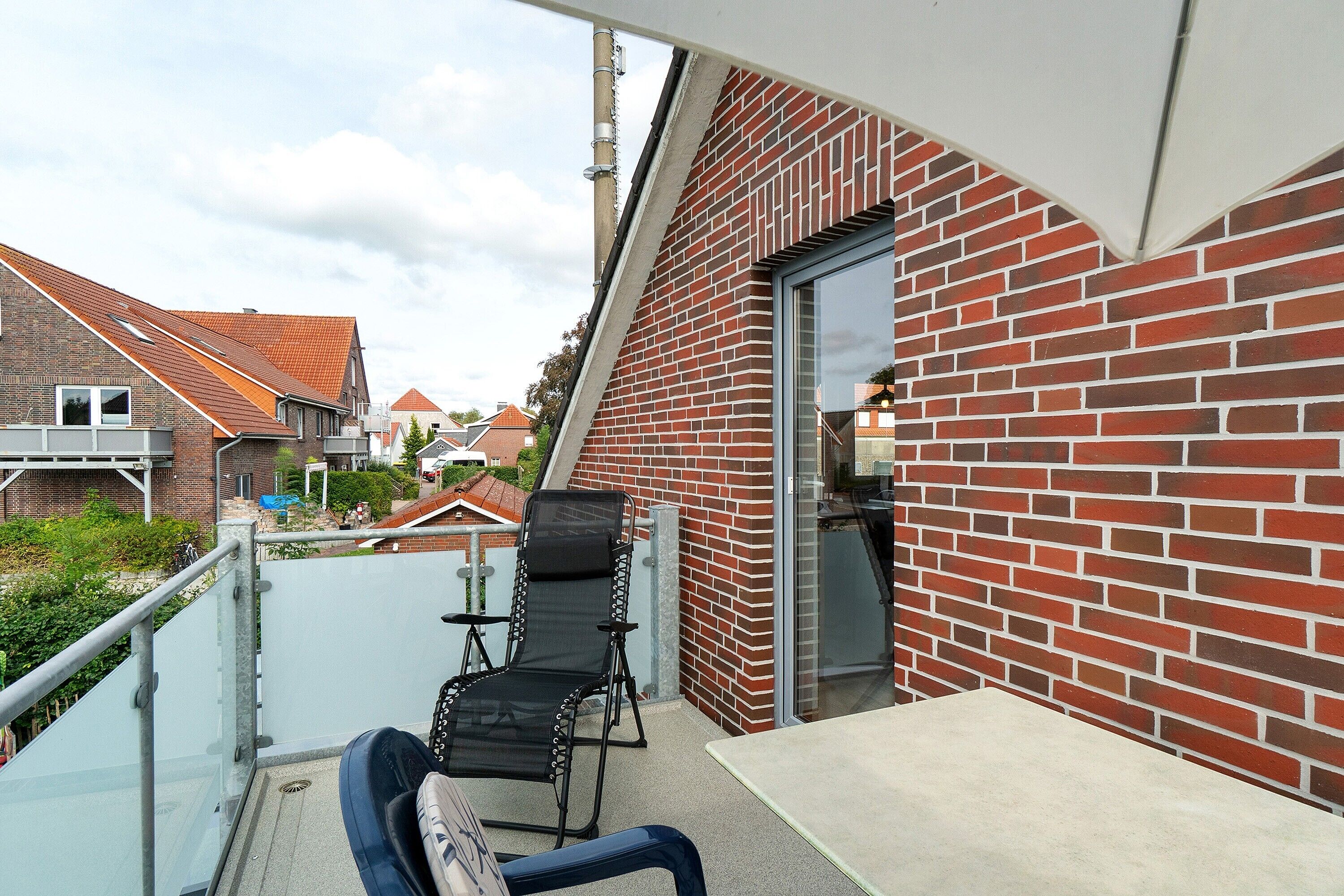 Ein Balkon mit schwarzem Stuhl und Tisch, einer roten Backsteinmauer und freiem Blick auf die Nachbarschaft.