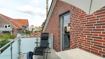Ein Balkon mit schwarzem Stuhl und Tisch, einer roten Backsteinmauer und freiem Blick auf die Nachbarschaft.