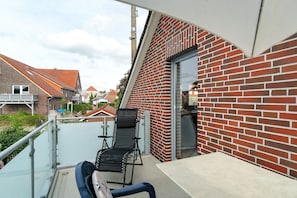Ein Balkon mit schwarzem Stuhl und Tisch, einer roten Backsteinmauer und freiem Blick auf die Nachbarschaft.