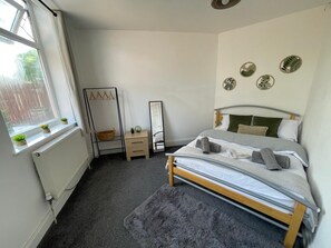 Un dormitorio con cama, cómoda, espejo y ventana con plantas.