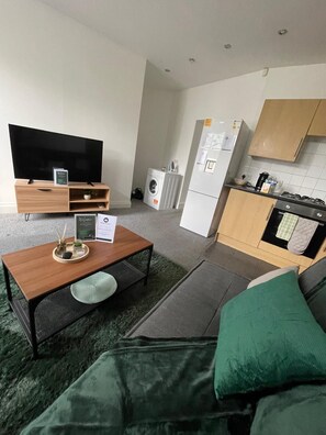 Un salón moderno con un televisor de pantalla plana, una mesa de centro de madera y un sofá verde.