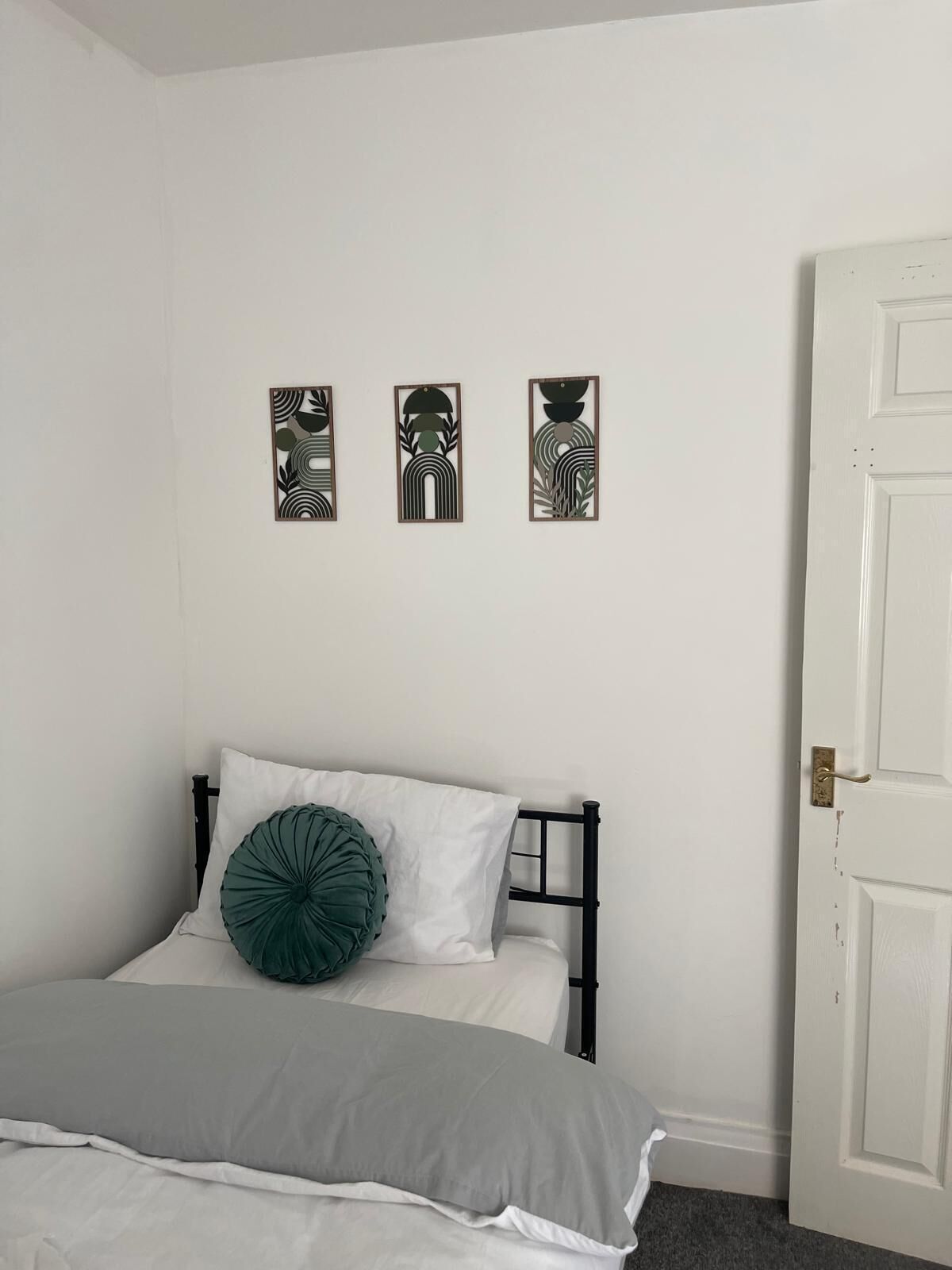 A bedroom with a bed, a door, and three wall-mounted artworks.