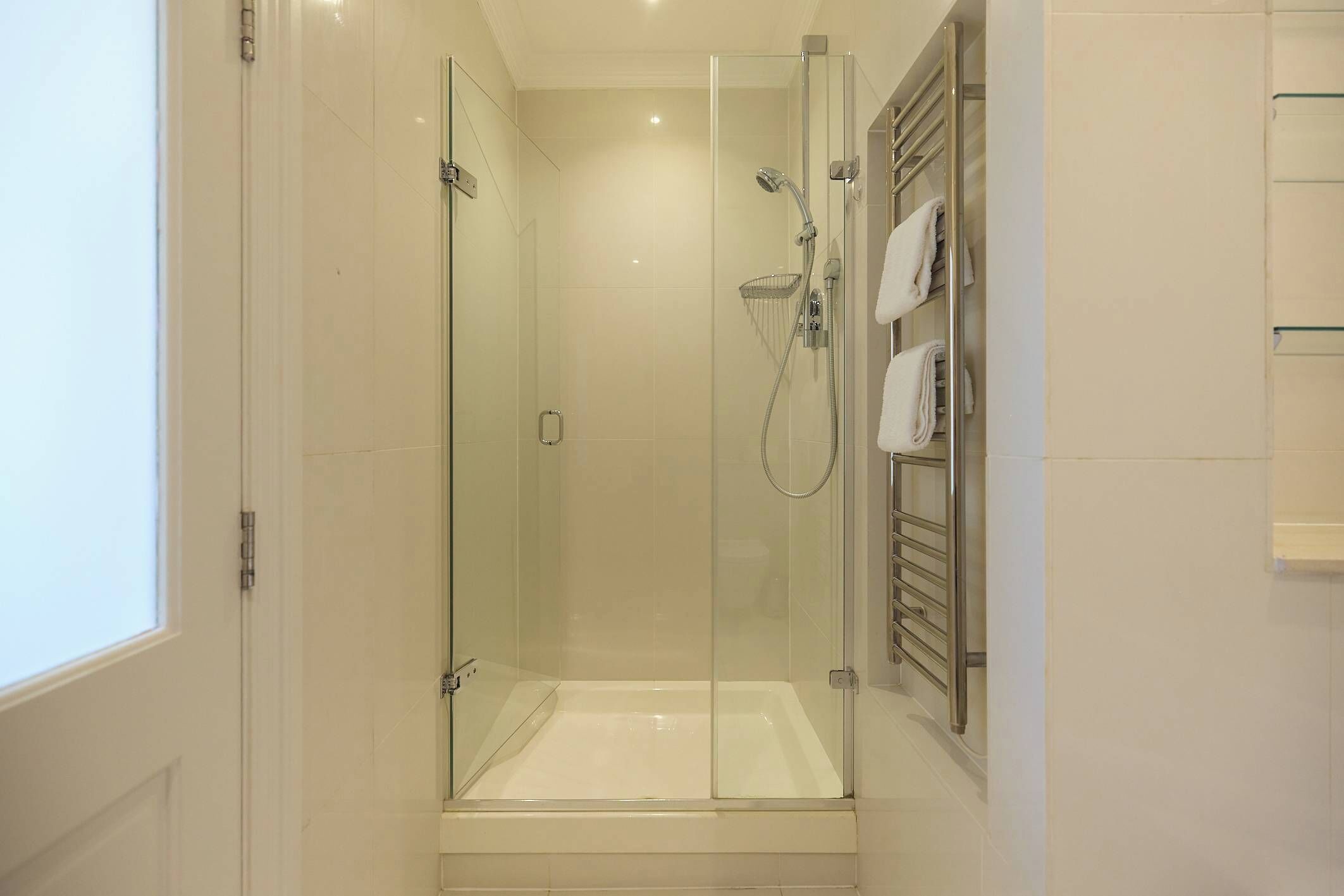 Une douche fermée par des parois en verre, dotée d’un pommeau de douche à main et d’un porte-serviettes fixé au mur.