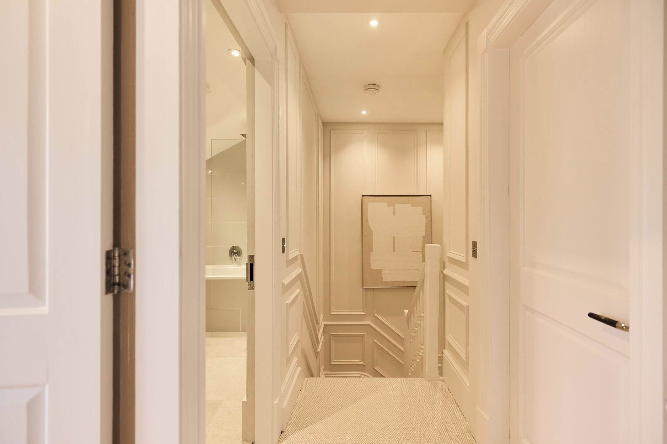 A hallway with a staircase leading to a bathroom, featuring white walls and doors.