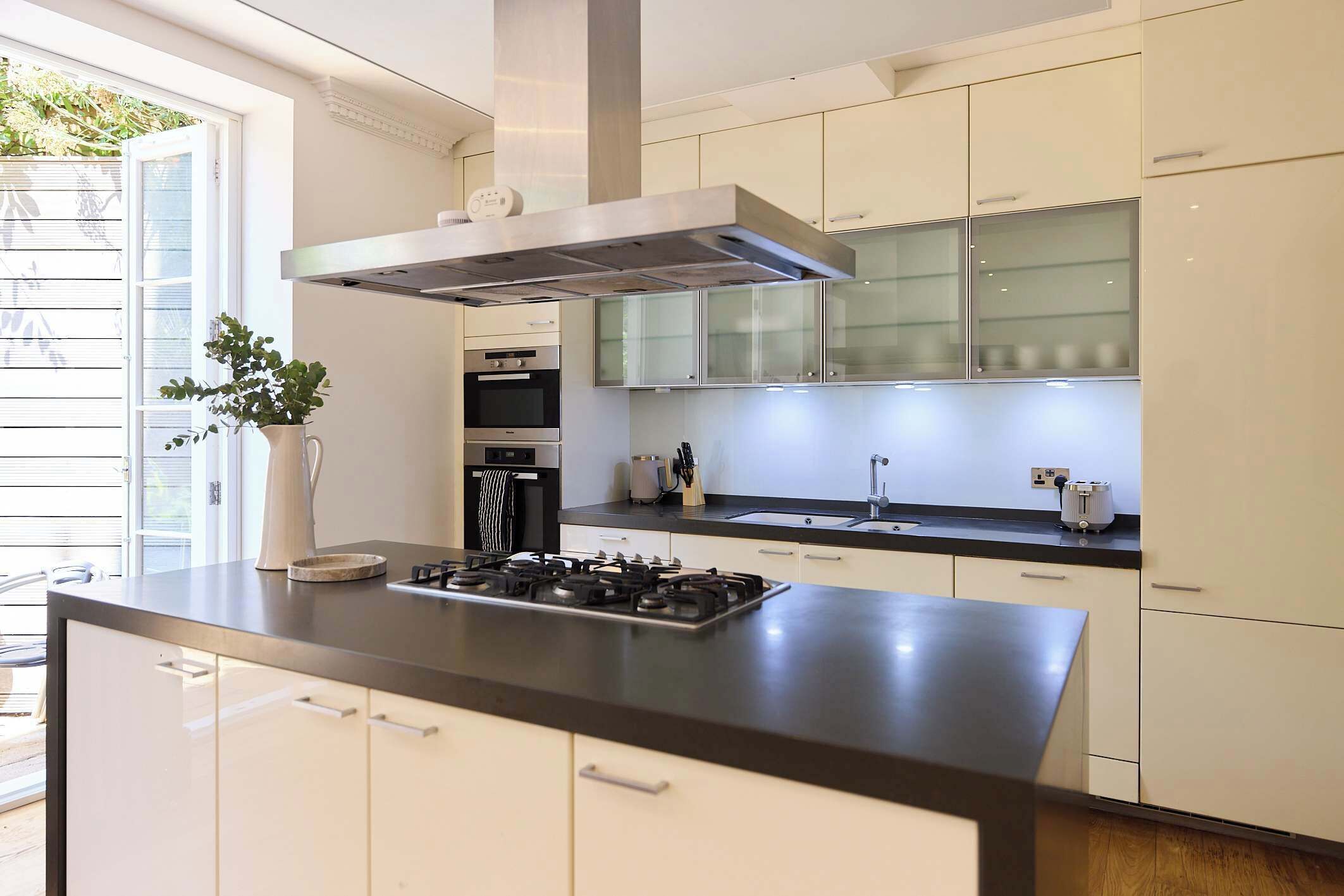A modern kitchen with a central island, stainless steel range hood, and white cabinetry.