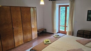Ein Schlafzimmer mit einem Bett, einem Holzschrank, einer Bank, einem Nachttisch und einem Fenster mit Vorhängen.