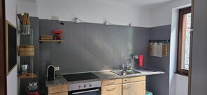 Cozinha compacta com azulejos cinzentos, pia, fogão e prateleiras de madeira.