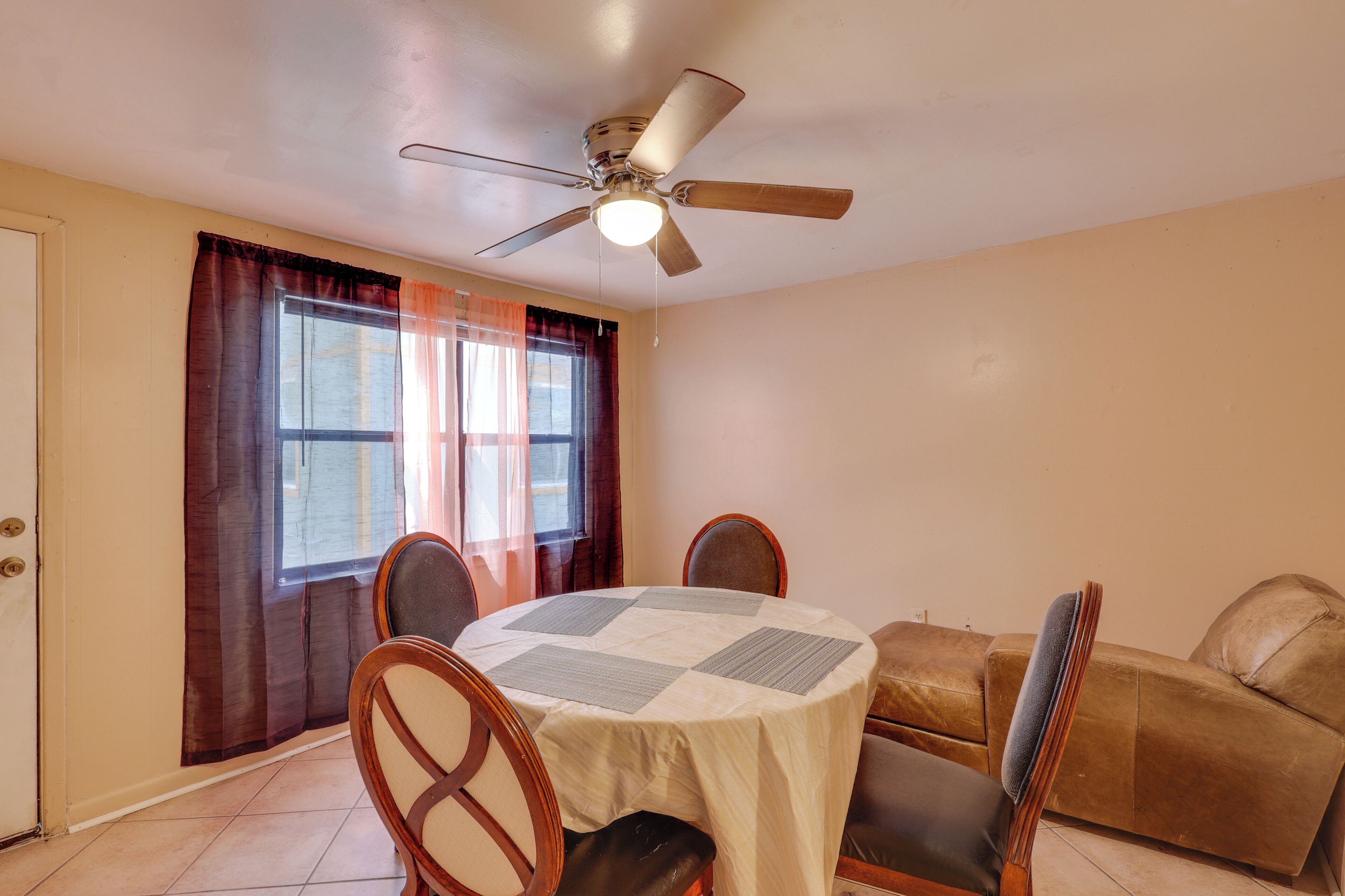 A dining area with a round table, chairs, a ceiling fan, and a window with curtains.