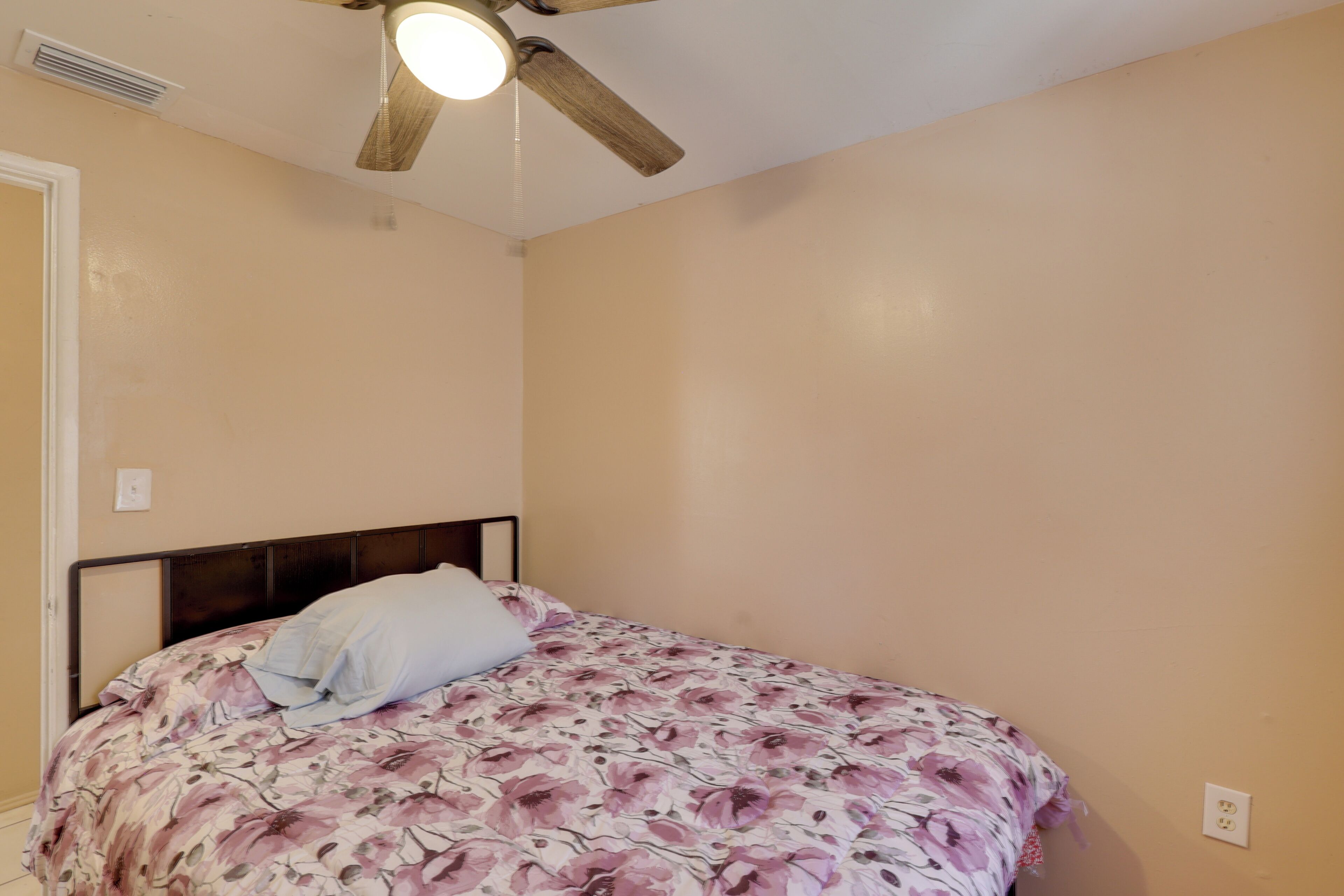 Ein Schlafzimmer mit einem Bett, einem Deckenventilator und einer Steckdose.