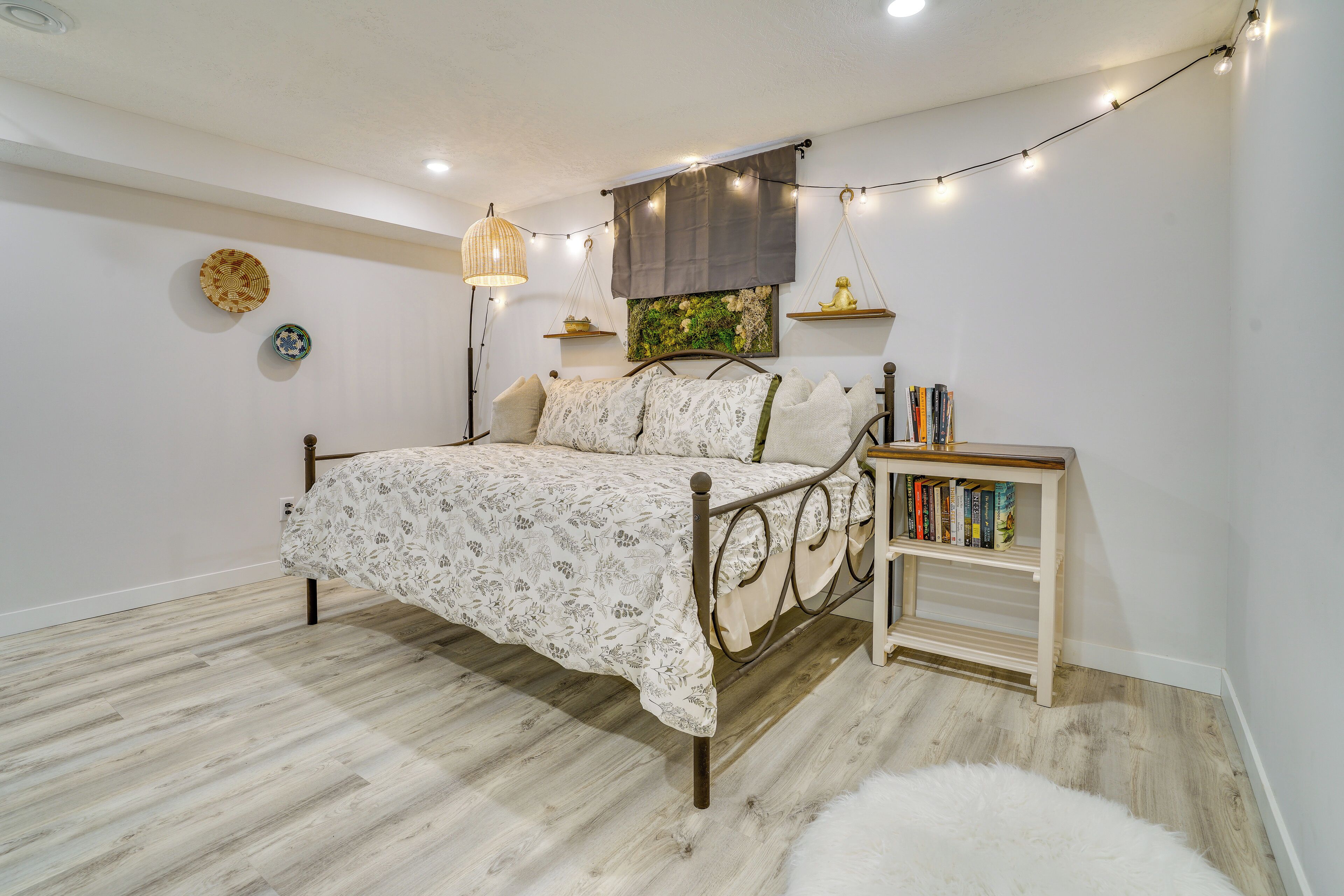A bedroom with a bed, bedside table, lamp, wall decorations, and a bookshelf.