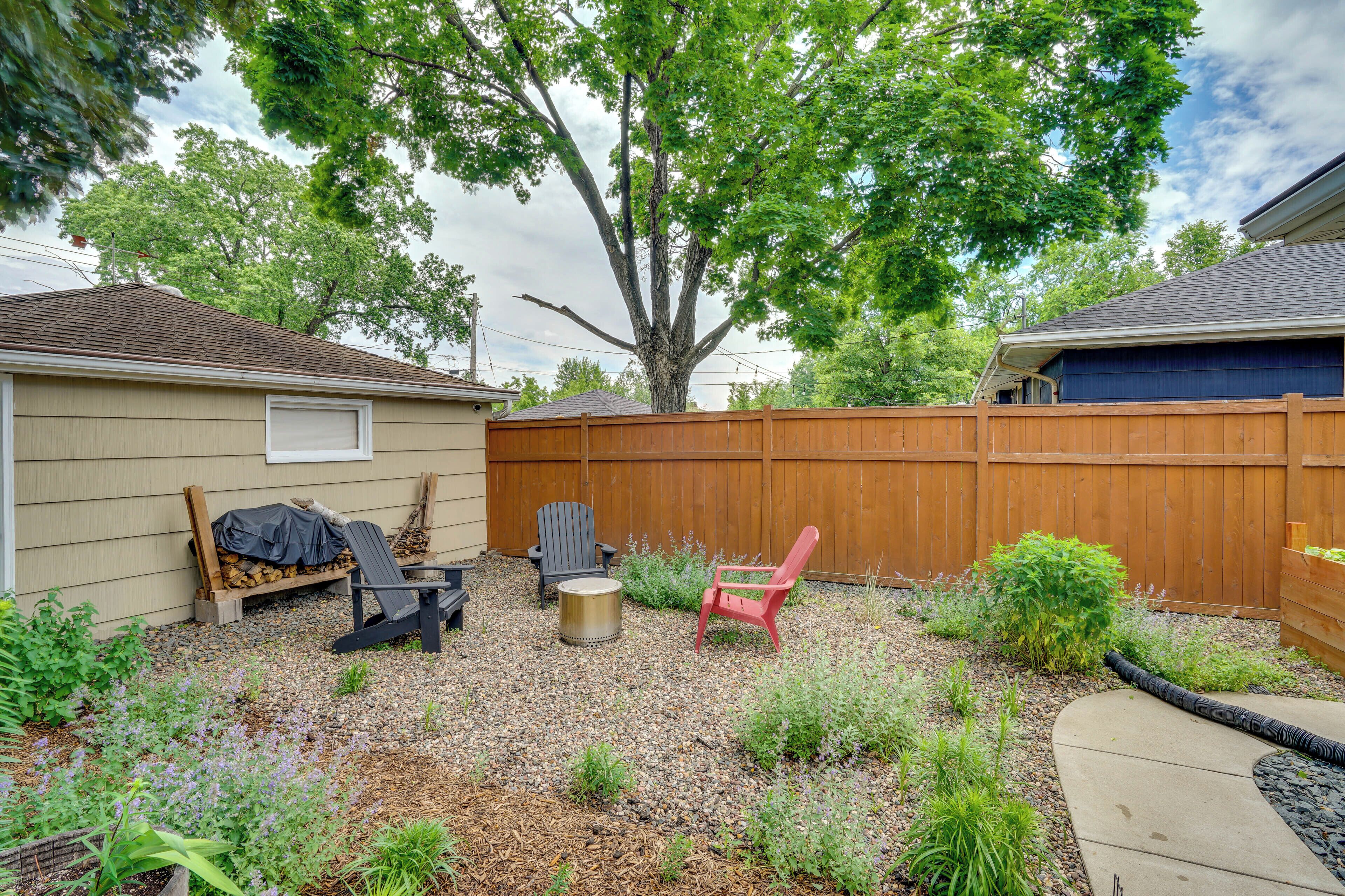 A backyard with a wooden fence, a tree, and outdoor furniture including a red chair and a blue chair.