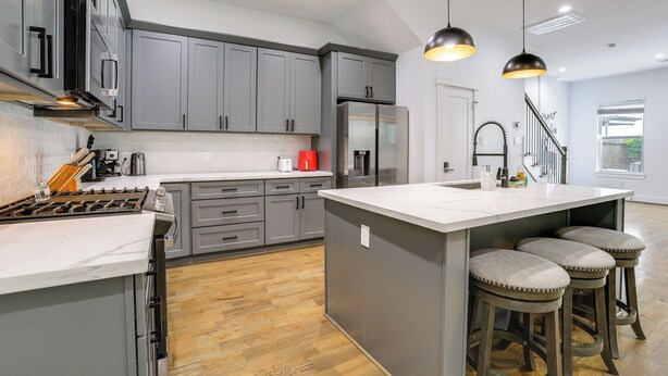 A modern kitchen with grey cabinets, a stainless steel refrigerator, a central island with stools, and pendant lighting. - Game Room & Private Yard! Family Escape in Houston (Houston)