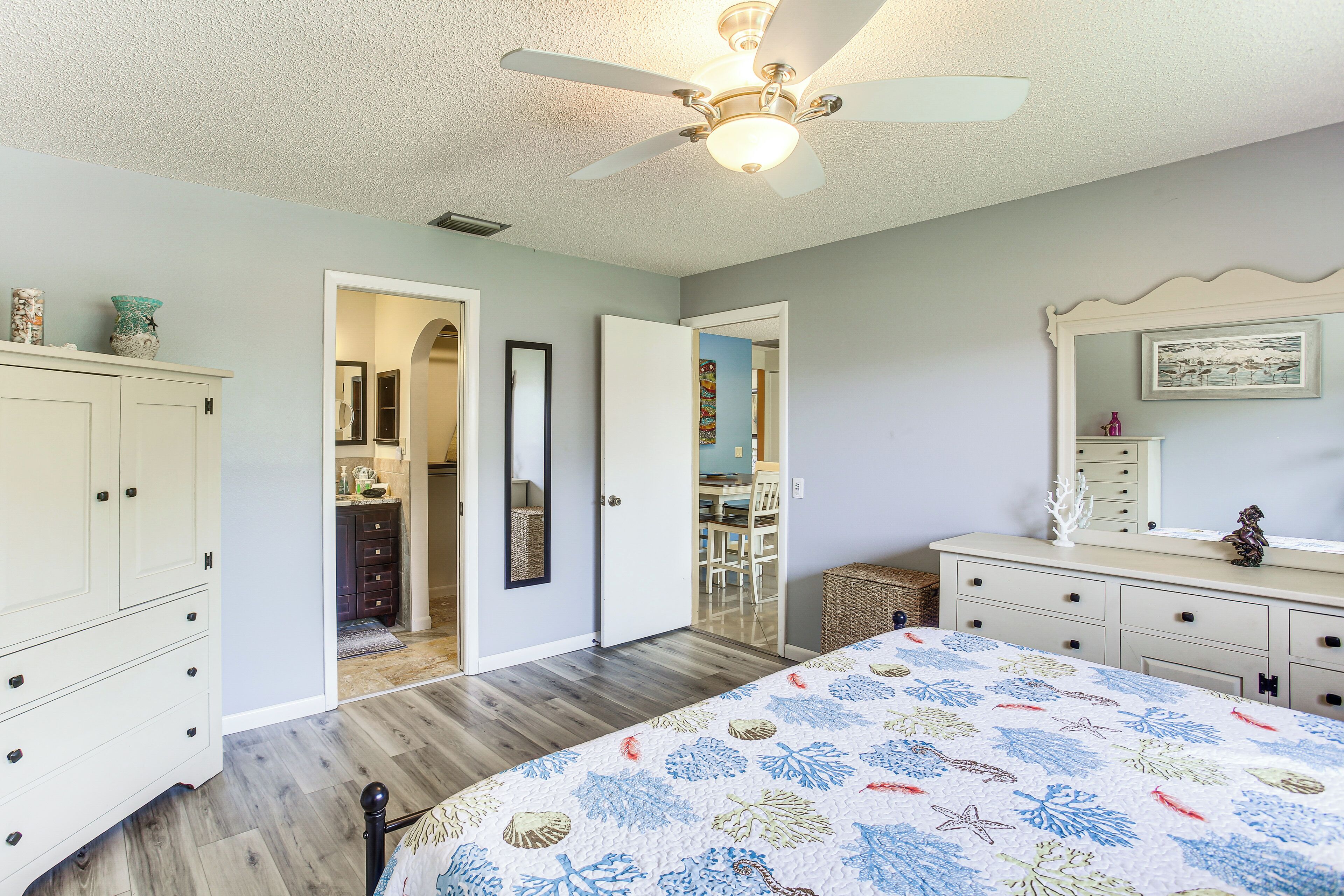 A bedroom with a bed, a ceiling fan, a dresser, and a door leading to another room.