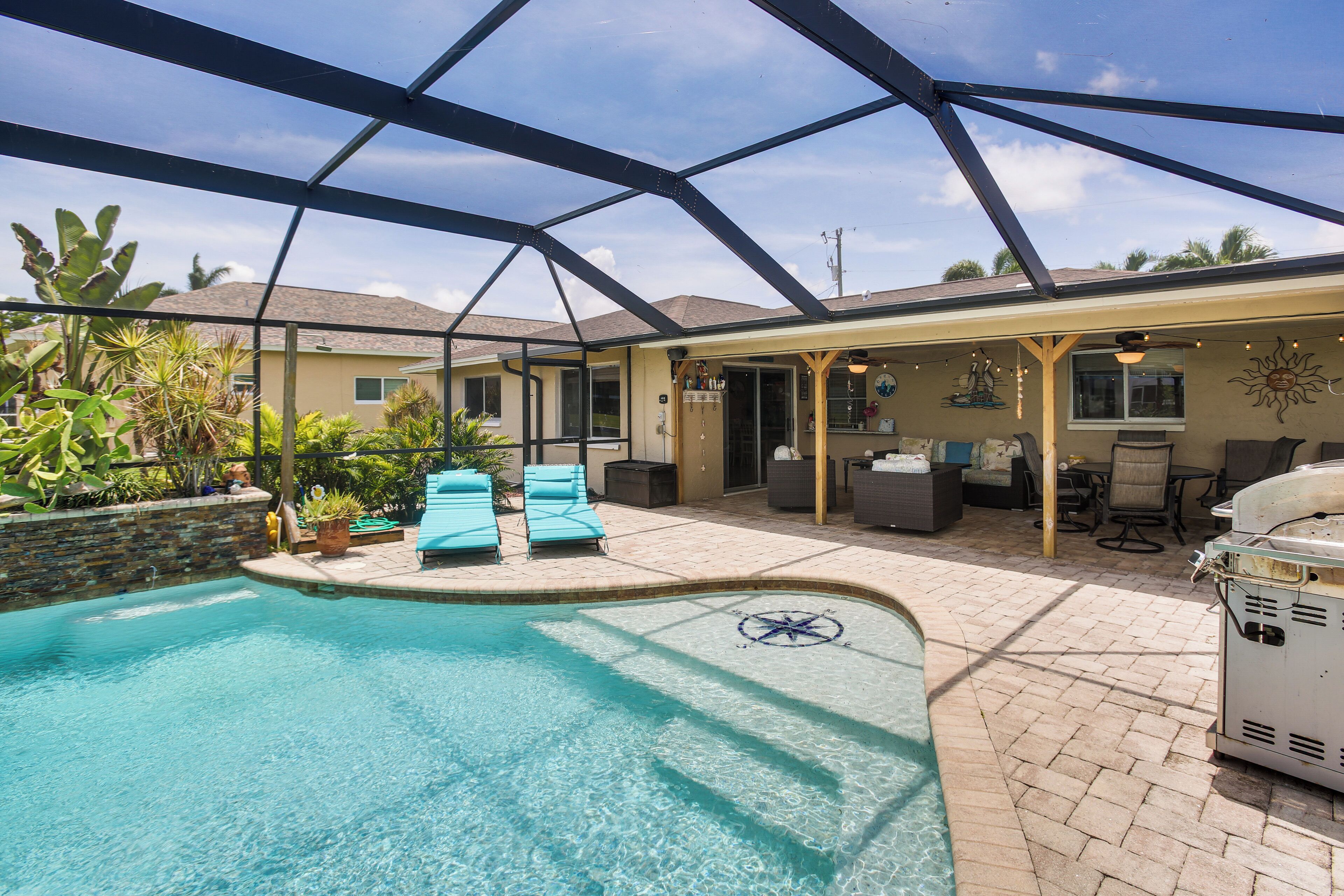 A pool area with a covered patio, lounge chairs, and a barbecue grill.