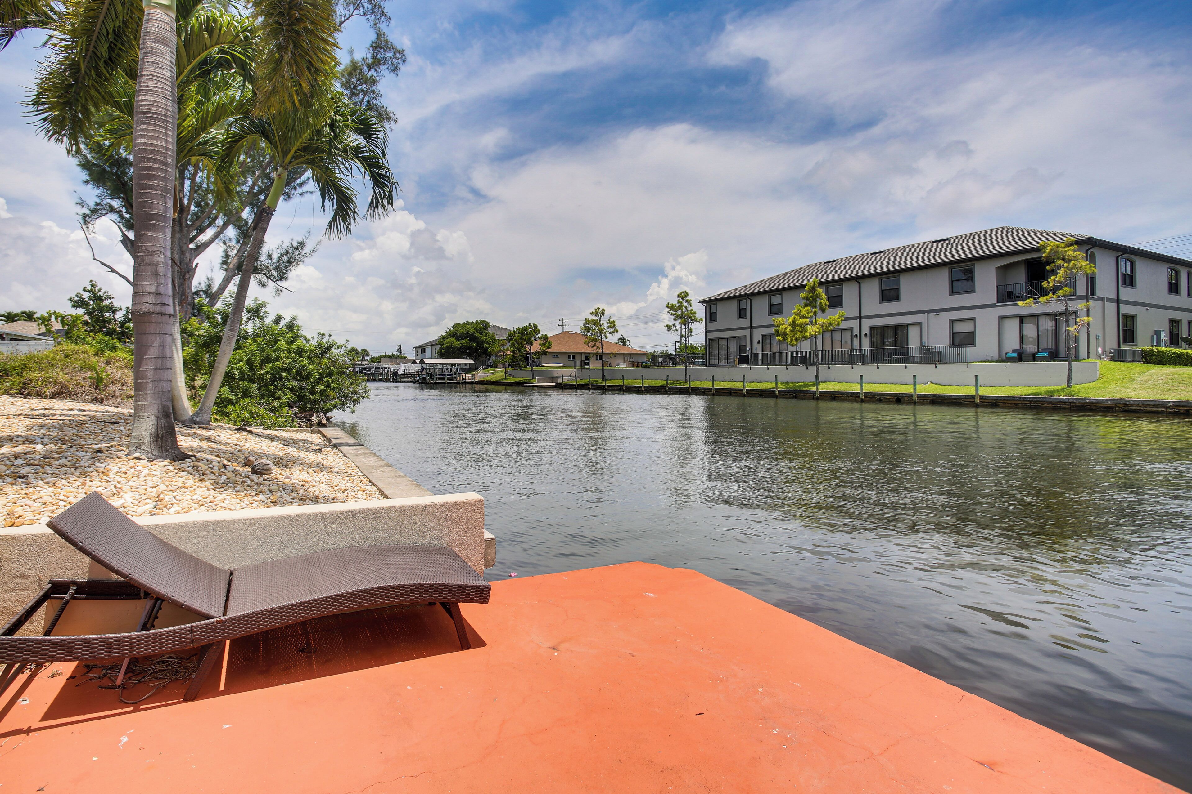 A waterfront property with a lounge chair, a calm water body, and a building with multiple windows and balconies.