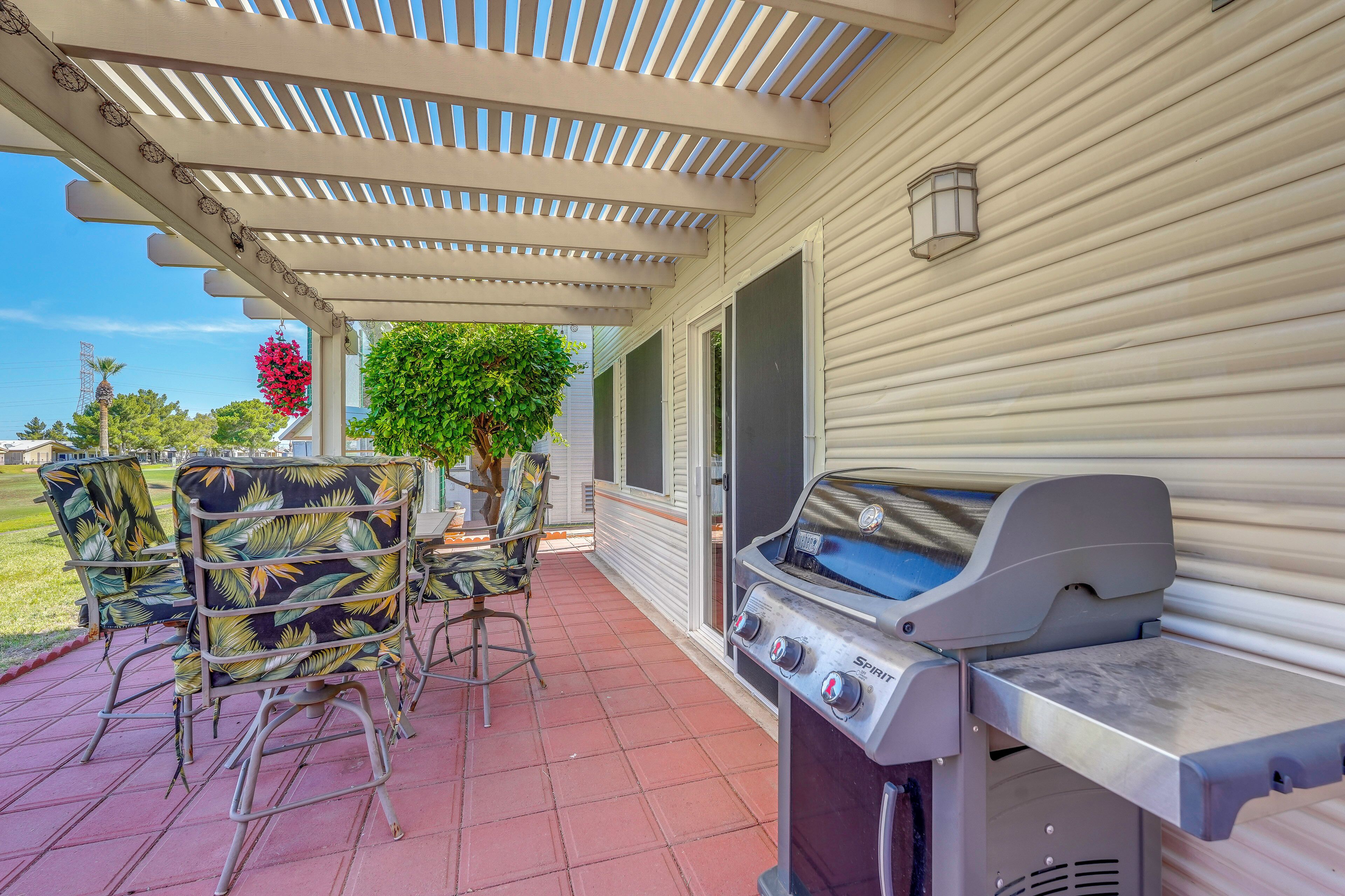 A covered patio with a grill, outdoor furniture, and a view of the house.