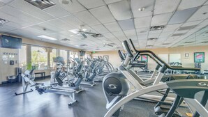 Une salle de sport équipée de divers appareils d’exercice, d’un ventilateur de plafond et d’une grande fenêtre laissant entrer la lumière naturelle.