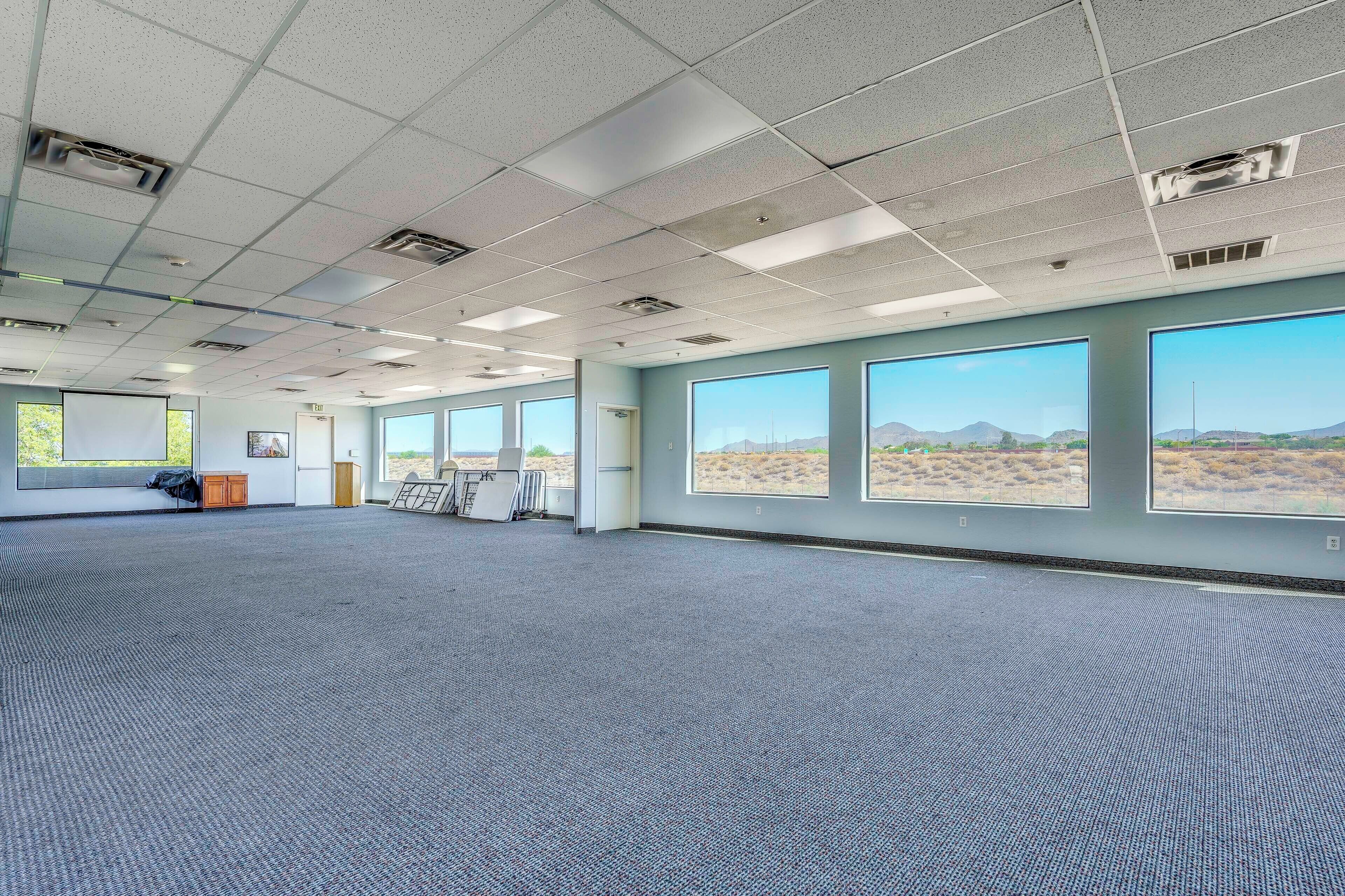 A spacious room with carpeted flooring, large windows, and a view of a desert landscape.