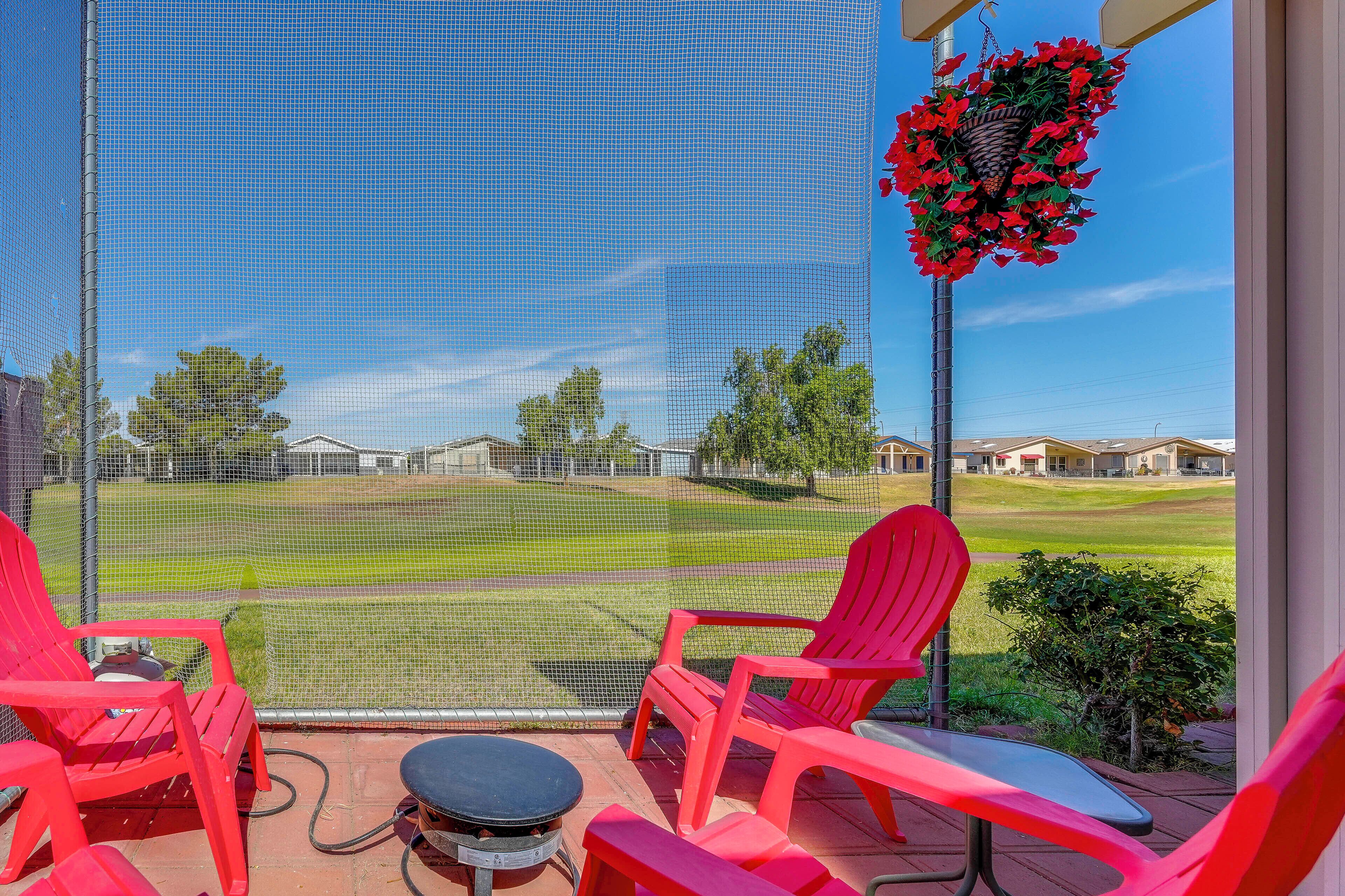A screened porch with red chairs and a table, overlooking a well-maintained lawn and houses.