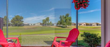 A screened porch with red chairs and a table, overlooking a well-maintained lawn and houses.