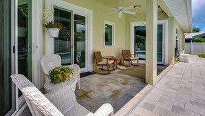 Eine überdachte Terrasse mit Korbmöbeln, Deckenventilator und Topfpflanzen.