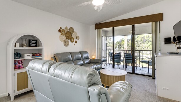 A living room with a grey leather sofa, a small round table, a bookshelf, and a decorative wall piece. - Resort Condo Near Anna Maria Island & IMG Academy (Bradenton)