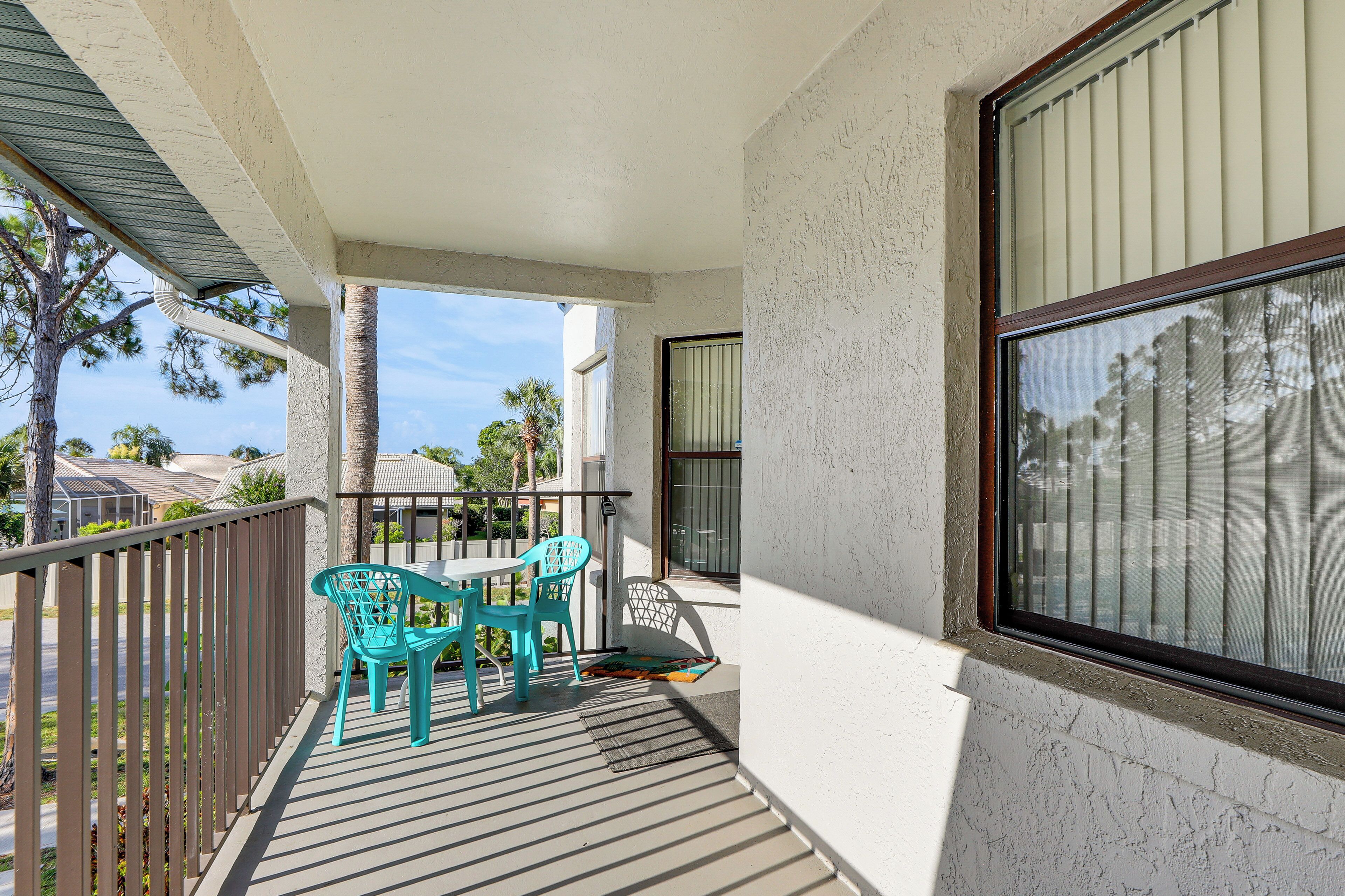 A balcony with a table and chairs, a view of the street, and a building in the background.