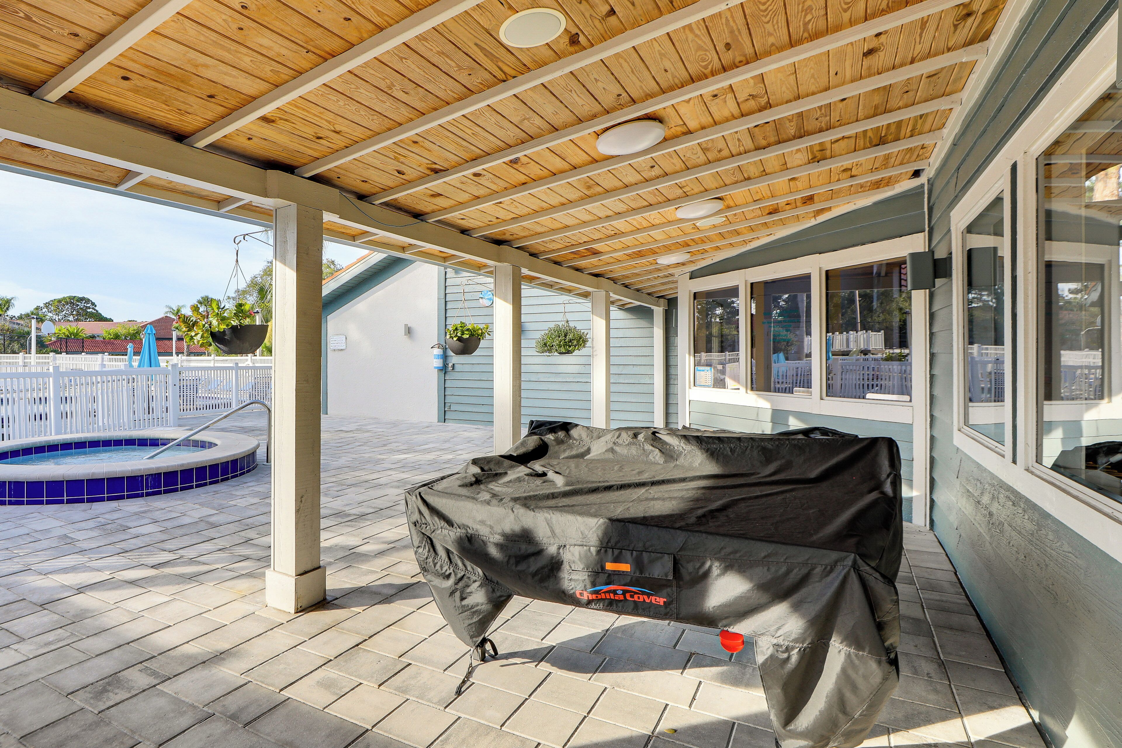 A covered outdoor area with a pool, wooden ceiling, and a covered grill.
