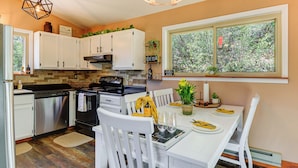 A modern kitchen with white cabinetry, a dining table set for two, and a window with a view of trees. - < 2 Mi to Whiskey Row! Mtn-view Adventure Basecamp (Prescott)